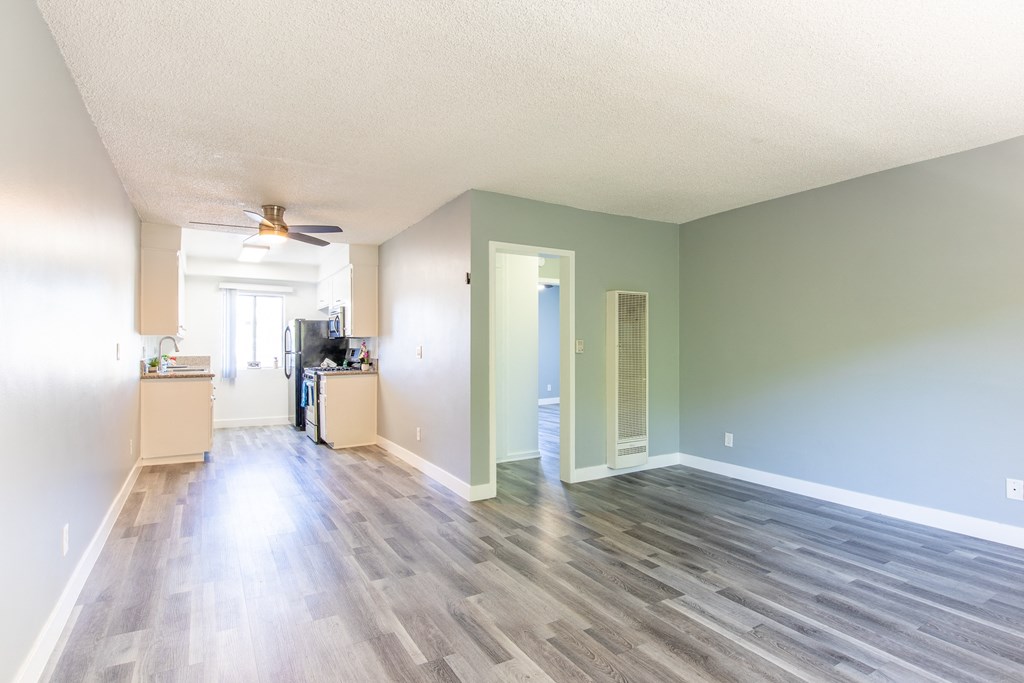 an empty living room and kitchen with wood floors and a ceiling fan