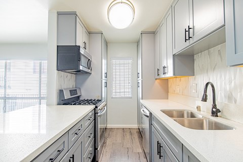 A kitchen with a white counter top and grey cabinets.