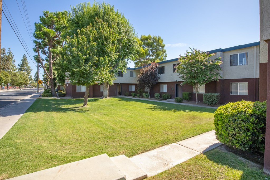 an apartment building with a lawn and trees in front of it