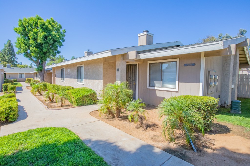 a beige house with a sidewalk and palm trees in front of it