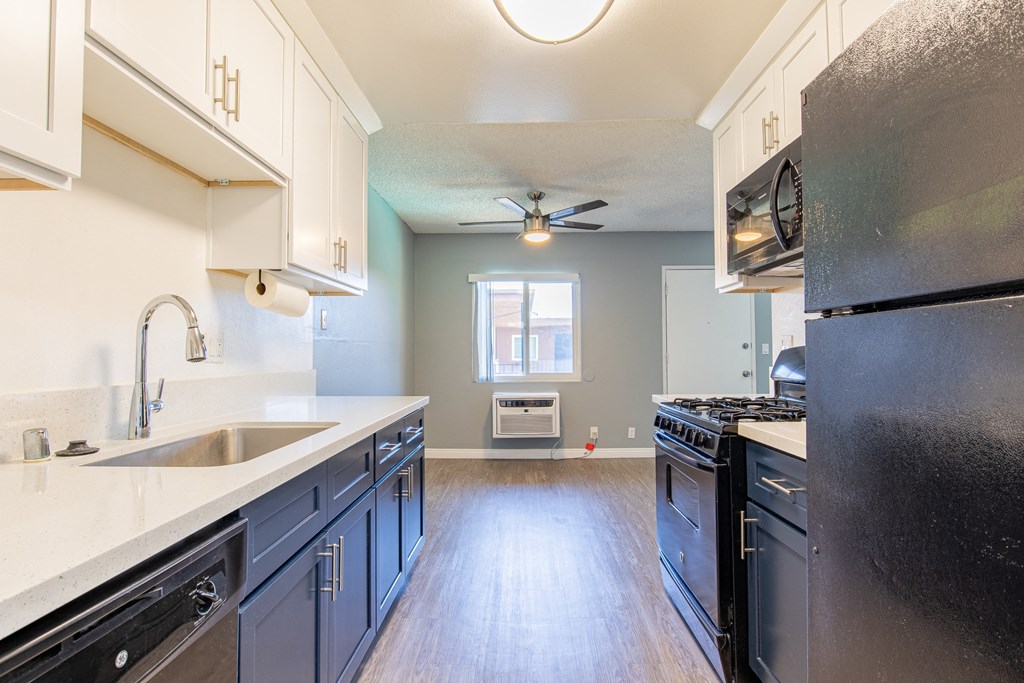 A kitchen with a black refrigerator and wooden floors.