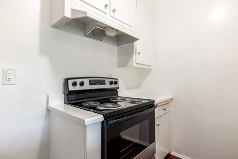 A white stove with a black oven sits under a vent in a kitchen.
