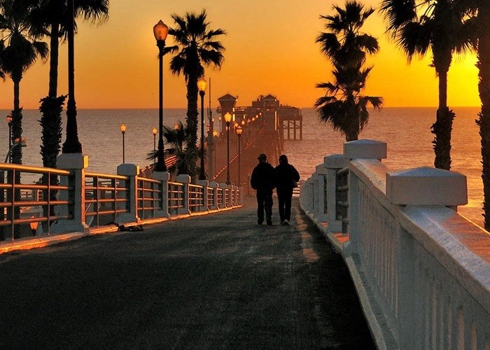 two people walking down a pier at sunset