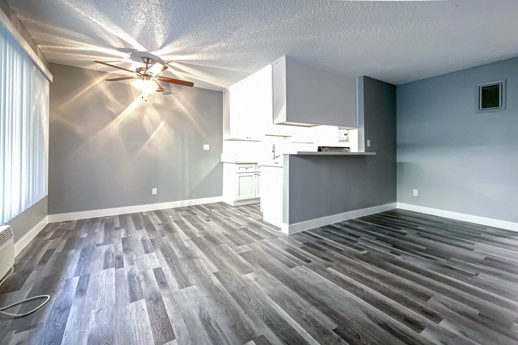 an empty living room with a kitchen and a ceiling fan