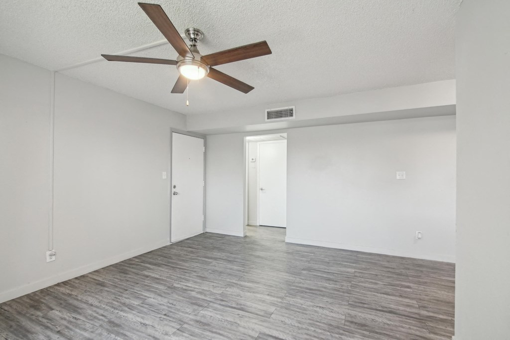 an empty living room with a ceiling fan and white walls