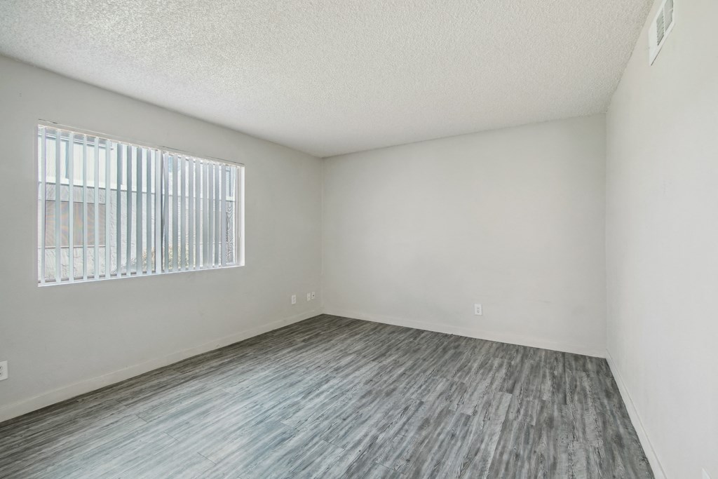 the spacious living room of an apartment with wood flooring and a window