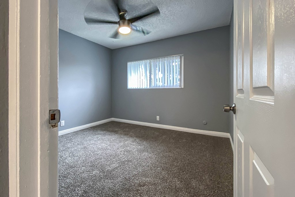 an empty living room with gray walls and a ceiling fan