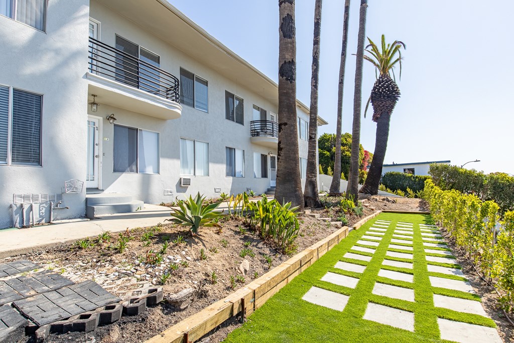 A white building with a balcony and a palm tree in front.