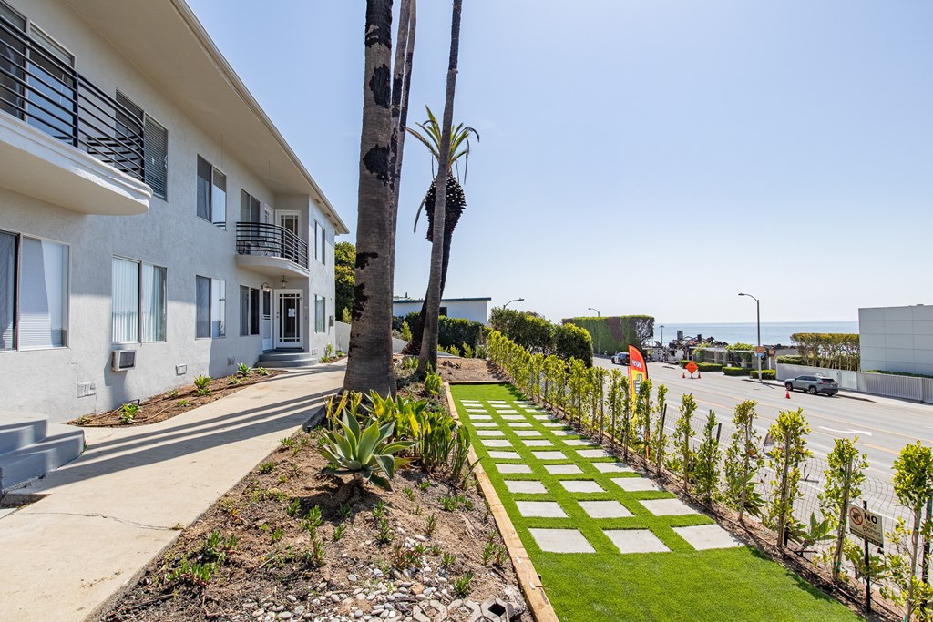 A white building with a balcony and a tree in front of it.