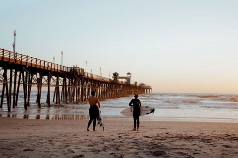 two men walking on the beach with their surfboards