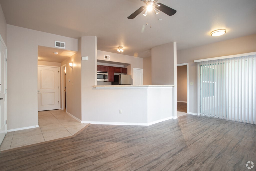an empty living room with a ceiling fan and a kitchen