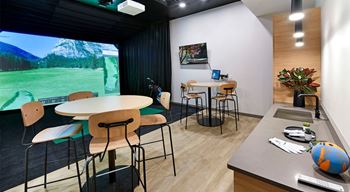 A room with a table, chairs, and a large screen displaying a mountainous landscape.