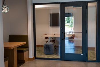 A glass door separates a room with a table and chairs from a hallway.