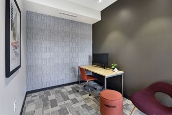 A room with a desk, chair, and a wall with a picture on it.