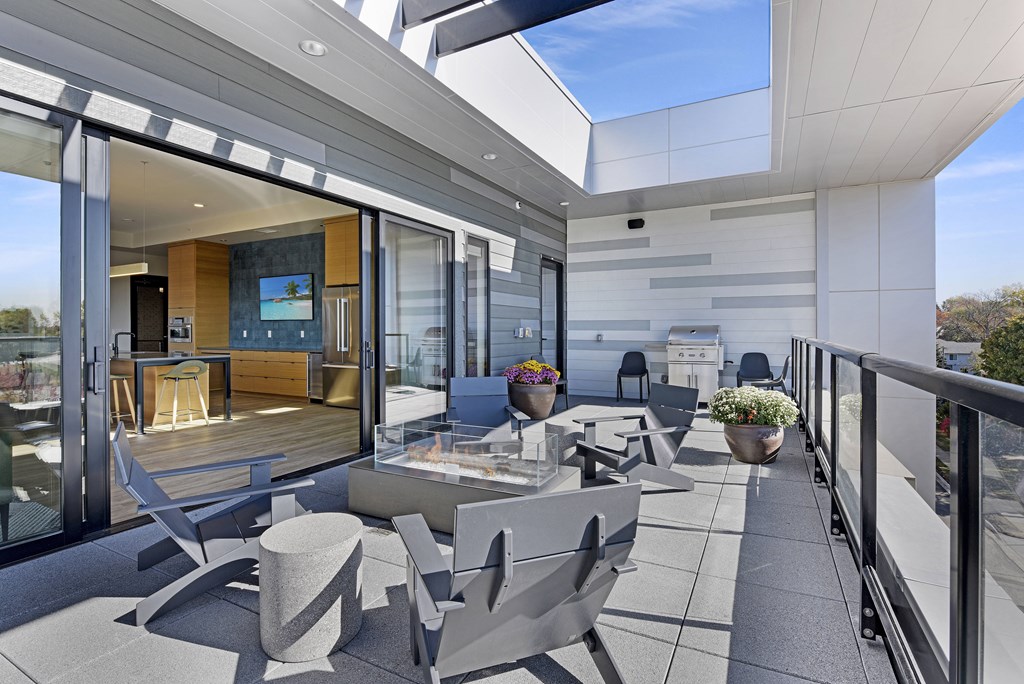 A modern balcony with grey furniture and a glass door leading to a living room.