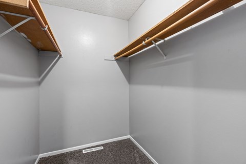 a walk in closet in a home with white walls and wood trim