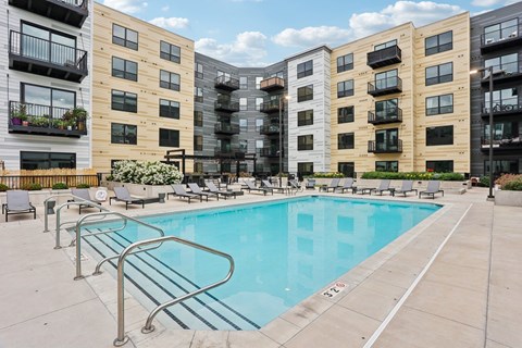 A swimming pool surrounded by apartment buildings and lounge chairs.