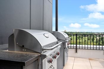 A stainless steel grill is on a balcony with a view of a green landscape.