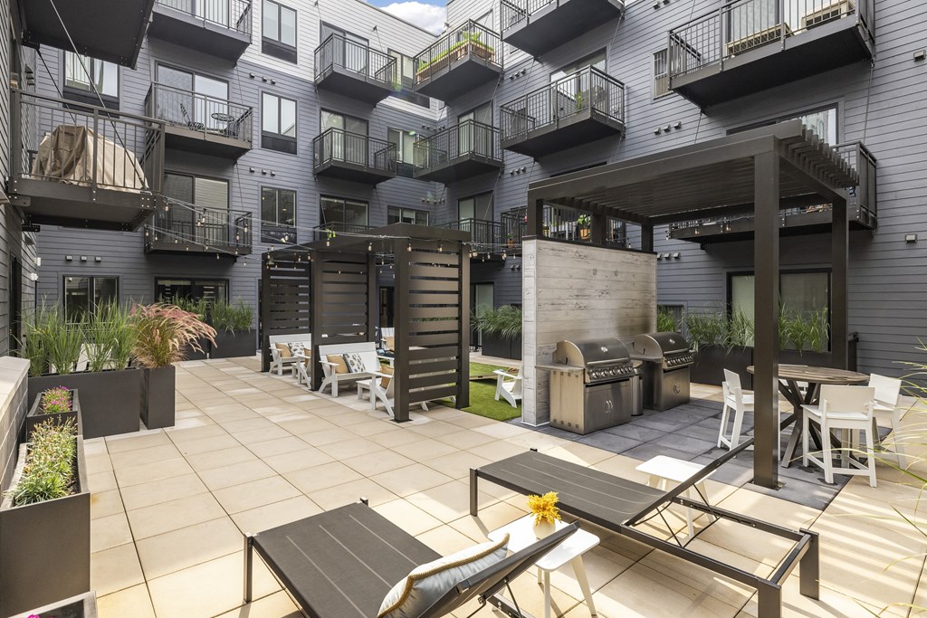 a patio with tables and chairs and a grill in front of an apartment building