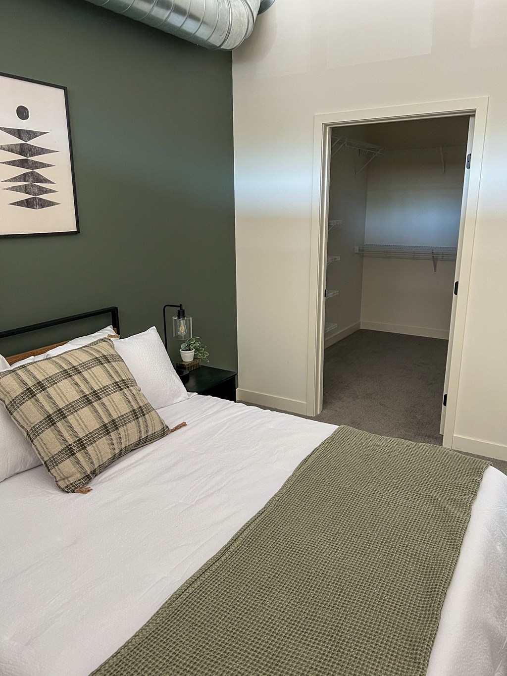 A bedroom with a bed and a pillow with a green wall and a painting.