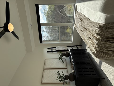 A room with a fan and a window showing a view of trees and a building outside.