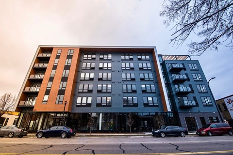 A modern multi-story apartment building with cars parked in front.