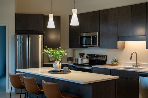 A kitchen with a refrigerator, microwave, oven, sink, and chairs.