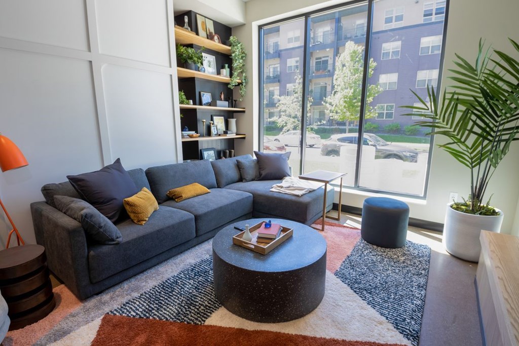 A living room with a grey couch, a round coffee table, and a large window.