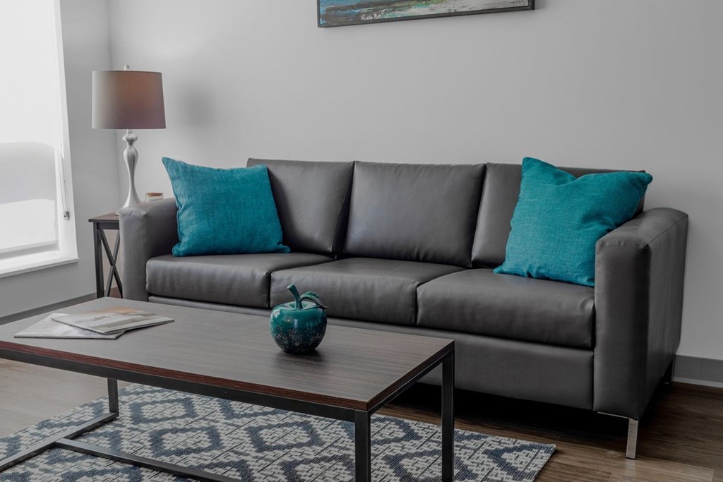 A grey couch with a blue pillow and a blue vase on a coffee table.