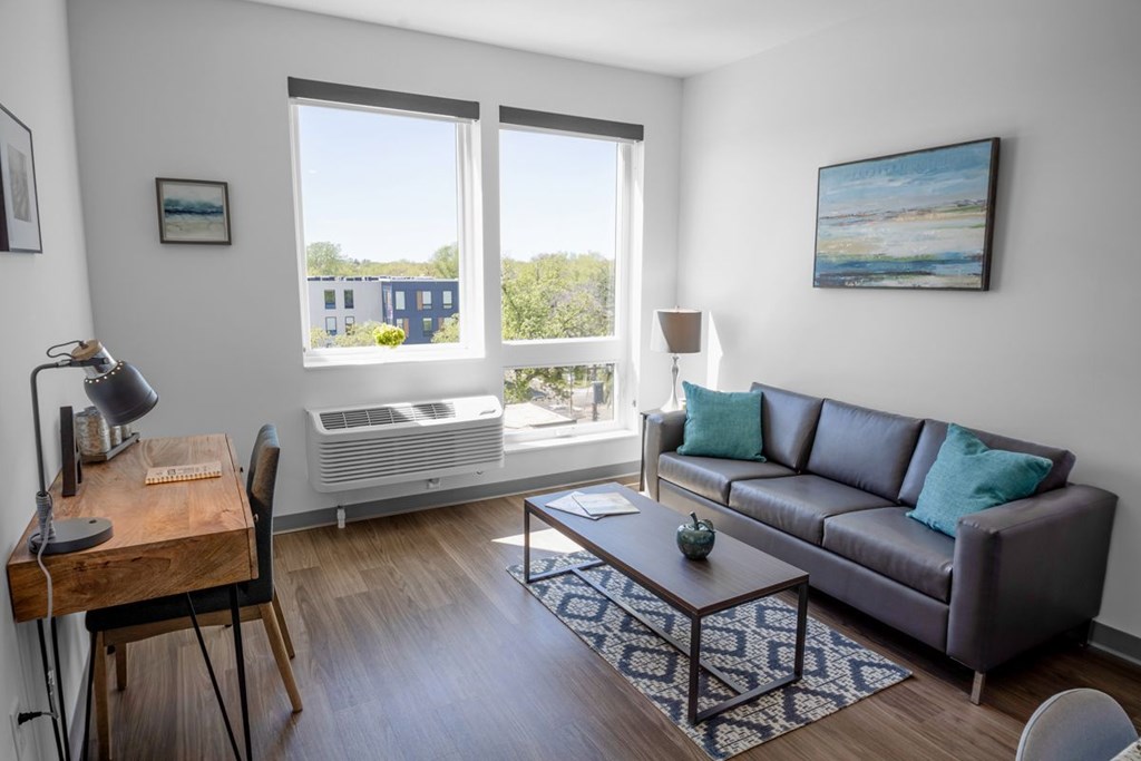 A living room with a brown couch, a wooden desk, and a painting on the wall.