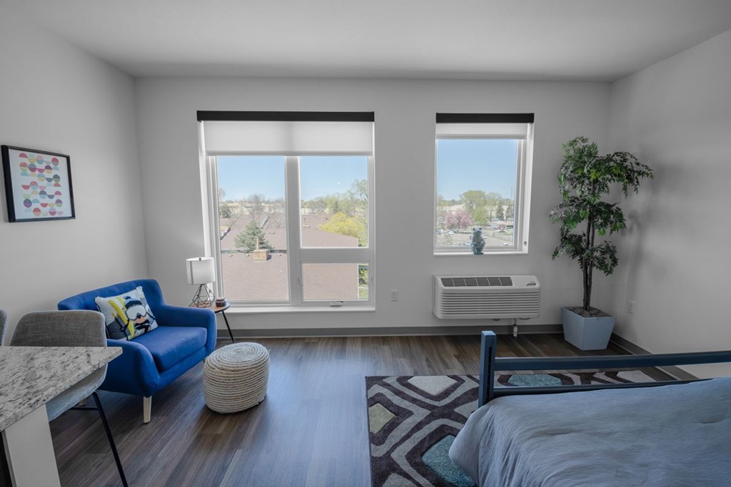 A bedroom with a blue couch and a large window with a view of trees and a building outside.