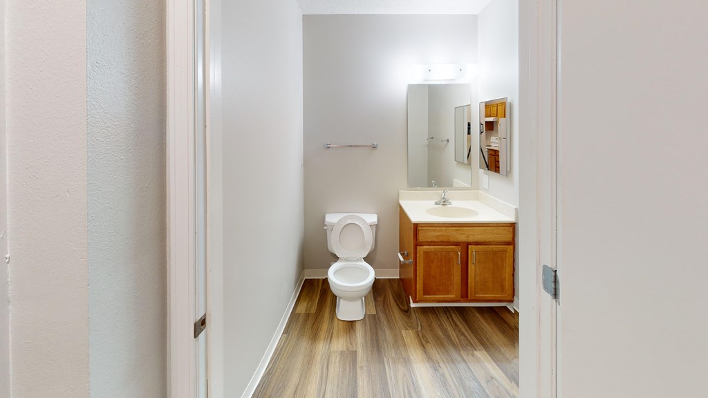 A white bathroom with wood flooring and a wooden cabinet.