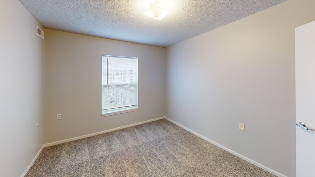 A room with a window and a carpeted floor.