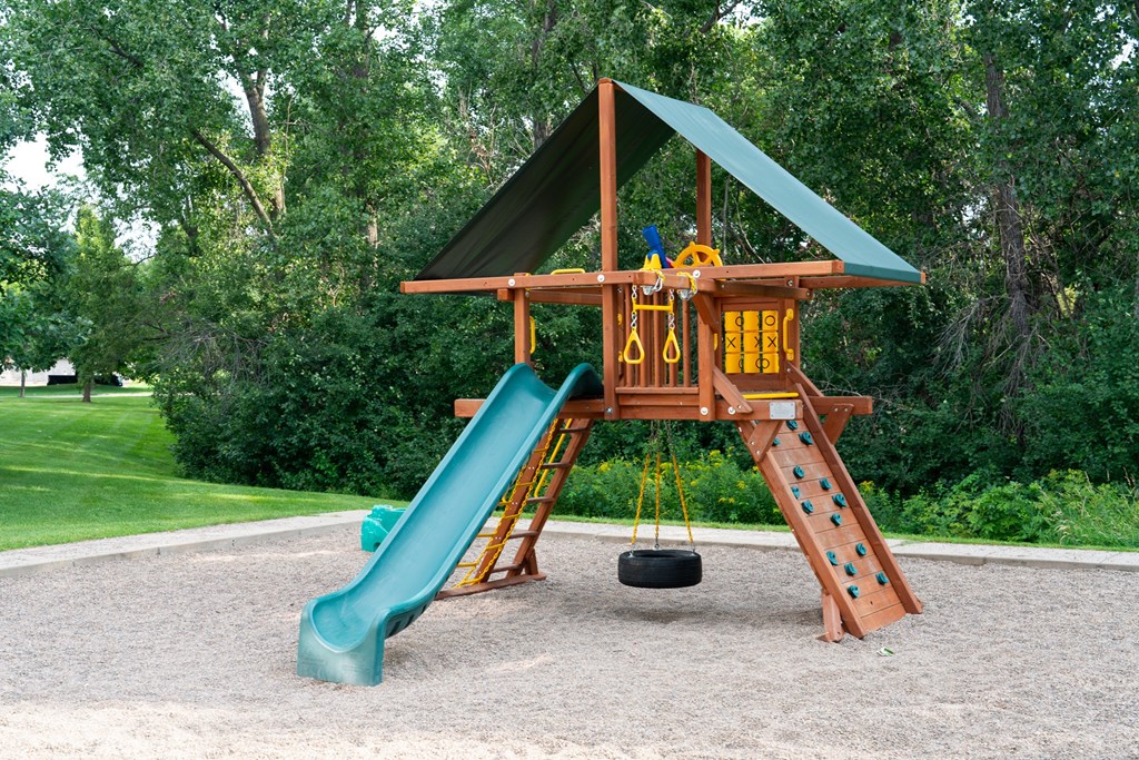 A playground with a green slide and a yellow and brown wooden structure.