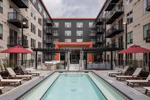 A swimming pool surrounded by lounge chairs and umbrellas in a courtyard.