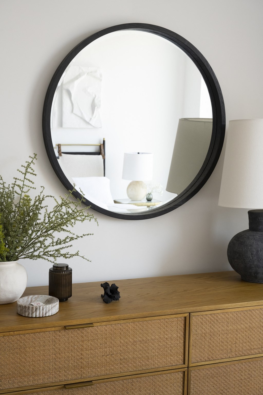 a round mirror above a dresser with a lamp on it