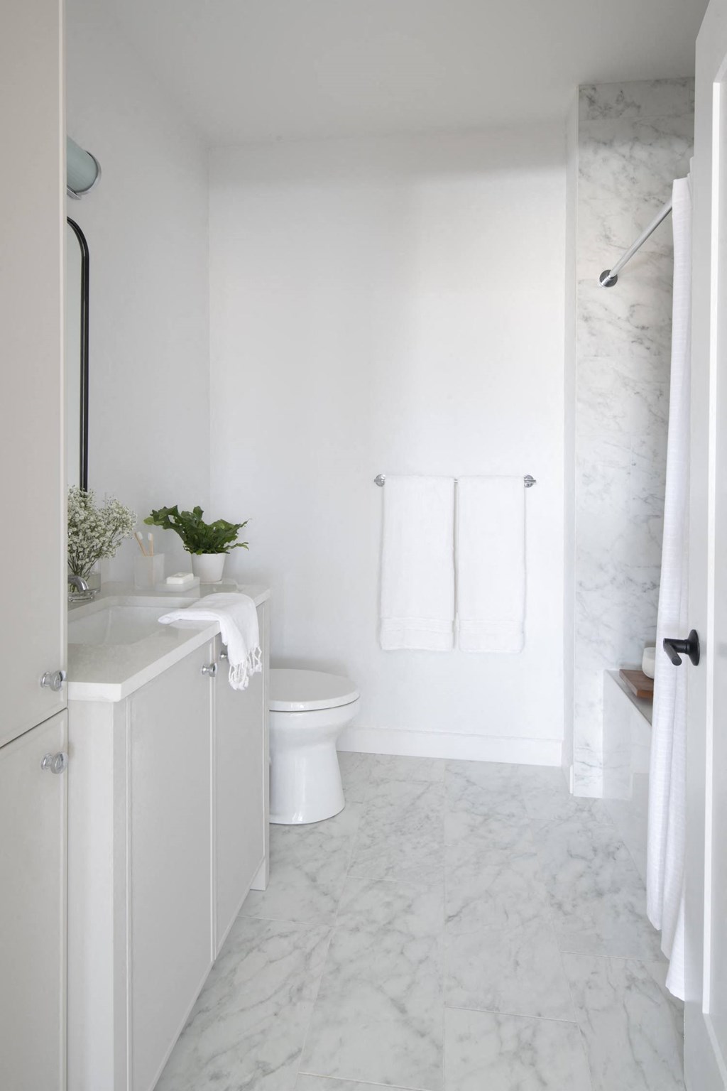 a white bathroom with a white sink and toilet and a white shower curtain