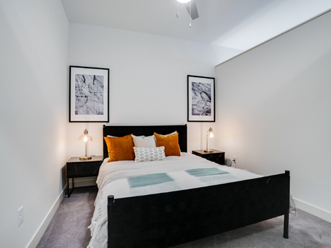a bedroom with a bed and two nightstands with orange pillows