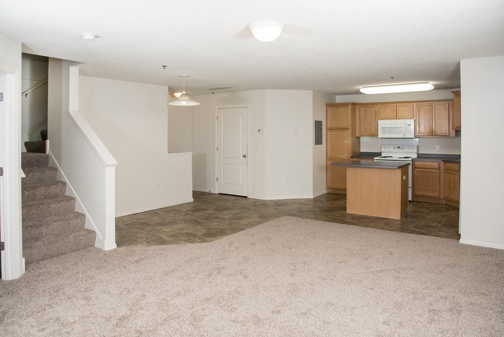 an empty living room and kitchen with a stairway to a room with wood cabinets