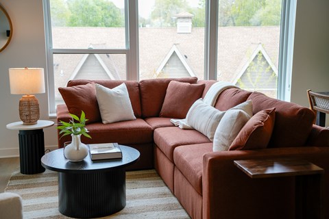 A living room with a red couch and a round table with a plant on it.