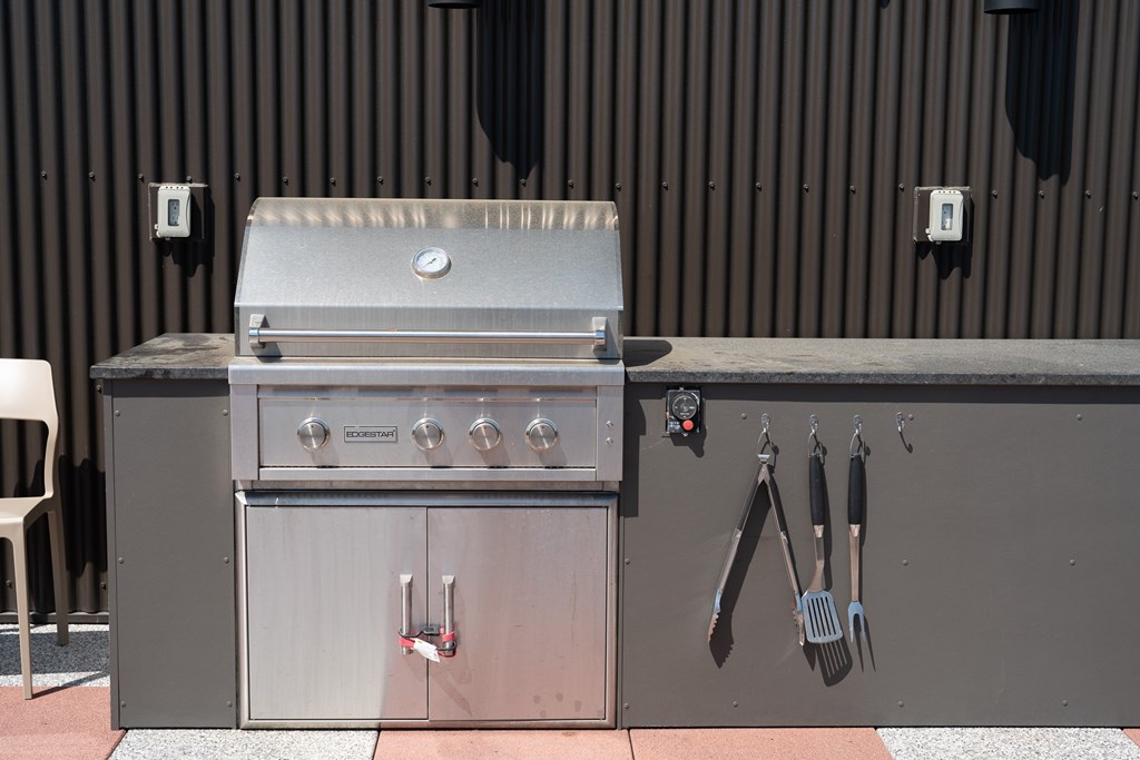 A stainless steel grill with utensils hanging on the wall.