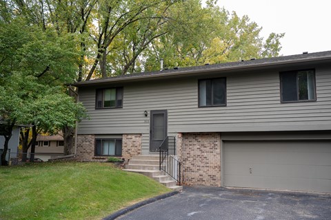 A house with a grey siding and a black door is surrounded by trees.