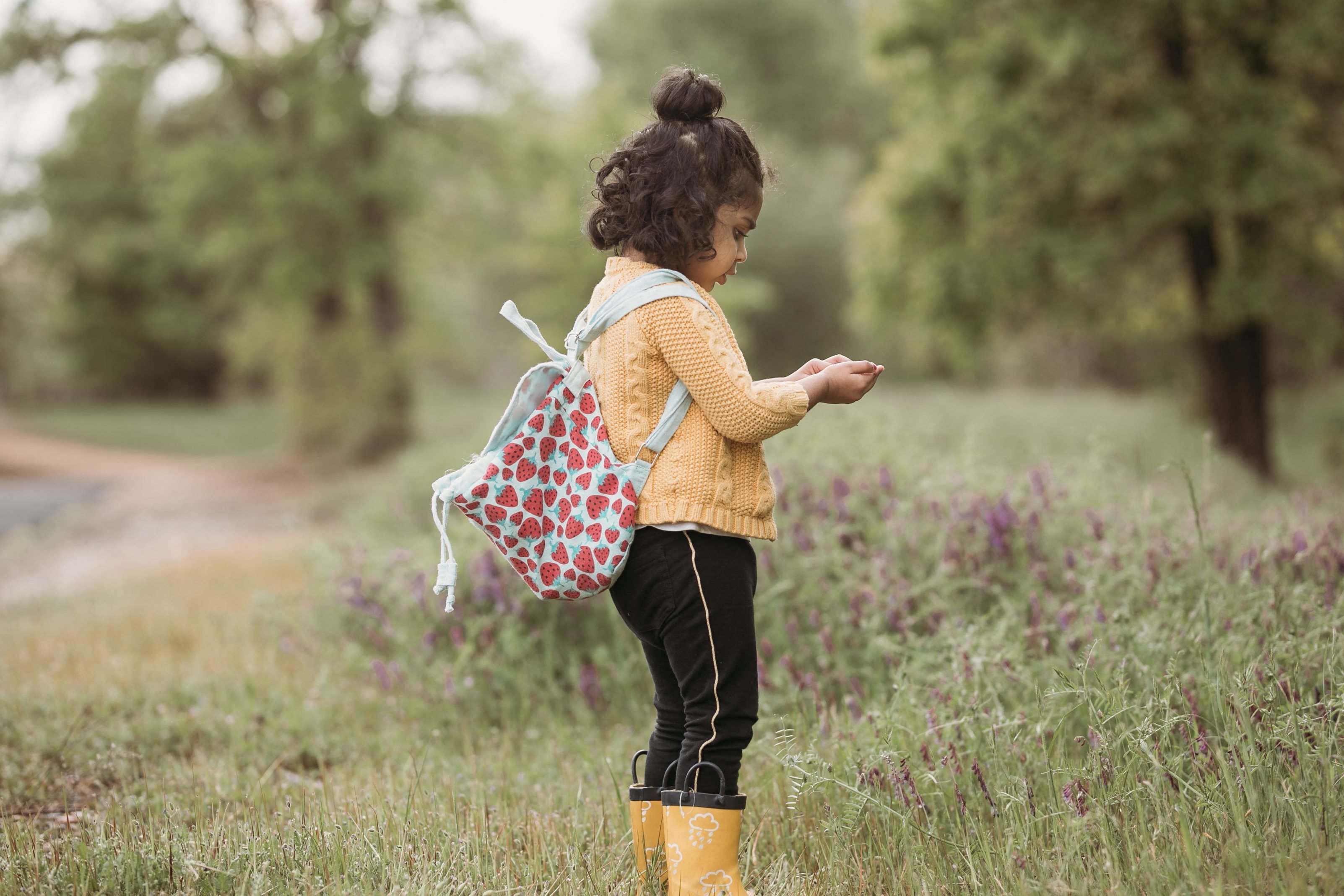 a little girl standing in a field holding a backpack