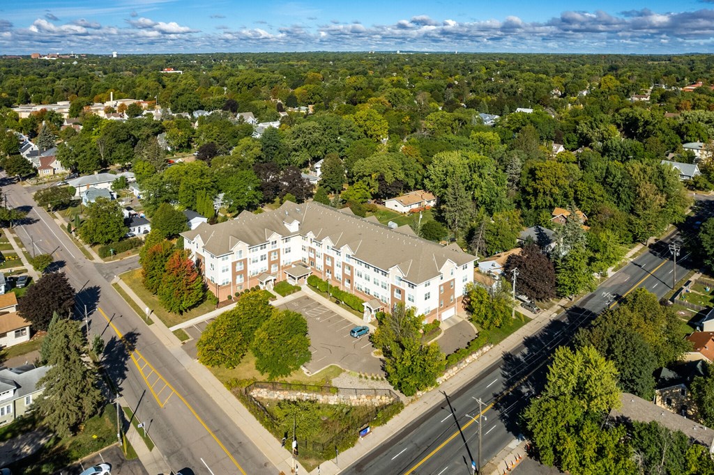An aerial view of a large white building surrounded by trees and a road in front.