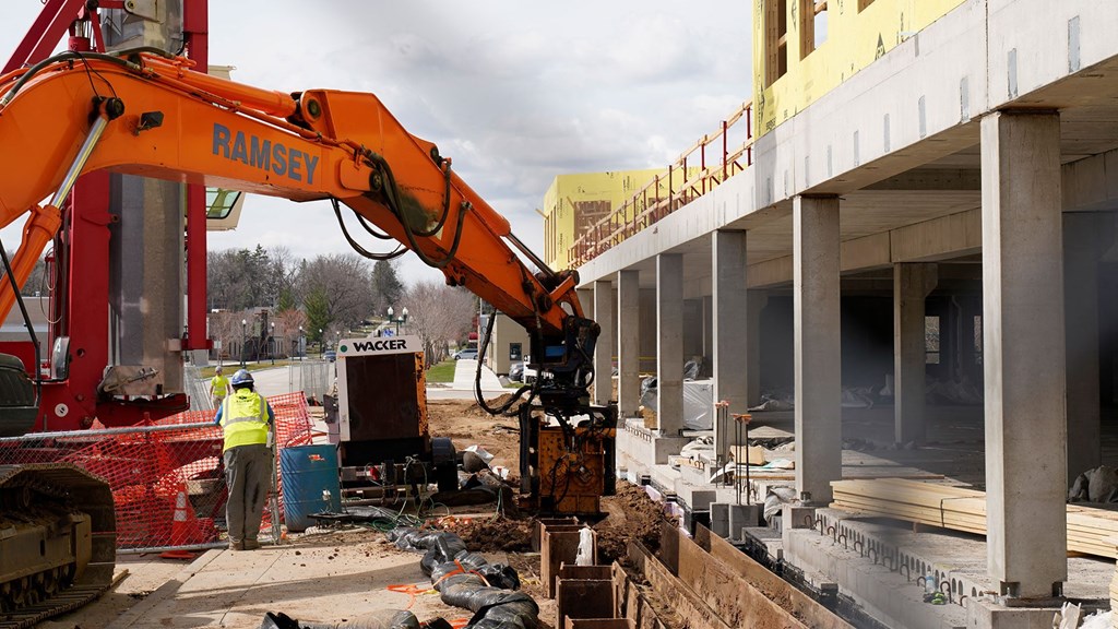 a construction worker stands next to an excavator outside of a building