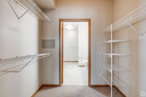 A walk-in closet with white shelving and a mirrored doorway.