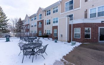 A snow-covered patio with a table and chairs in front of apartment buildings.