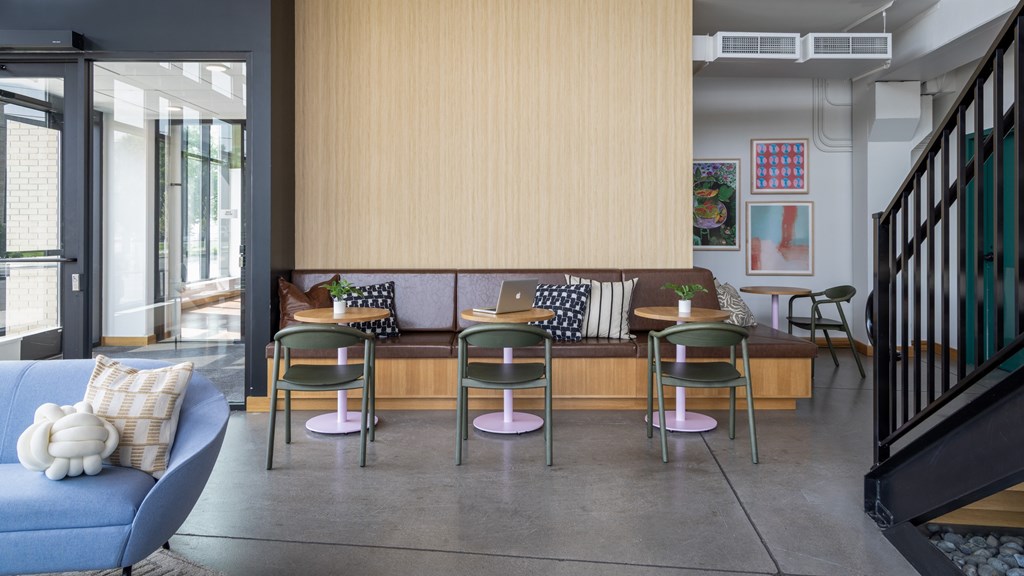 A blue sofa with a white pillow is in front of a wooden bench with four chairs around it.