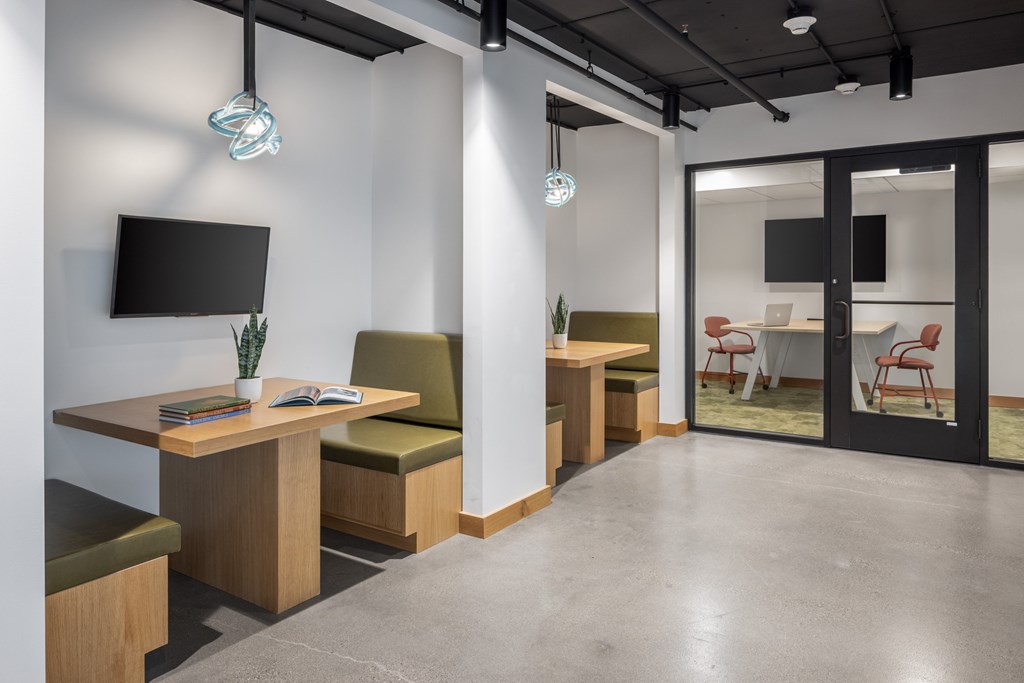 A modern office space with a TV mounted on the wall and a glass door leading to another room.