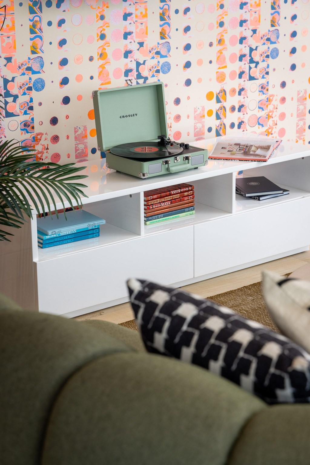 A record player sits on a shelf with books and a plant.